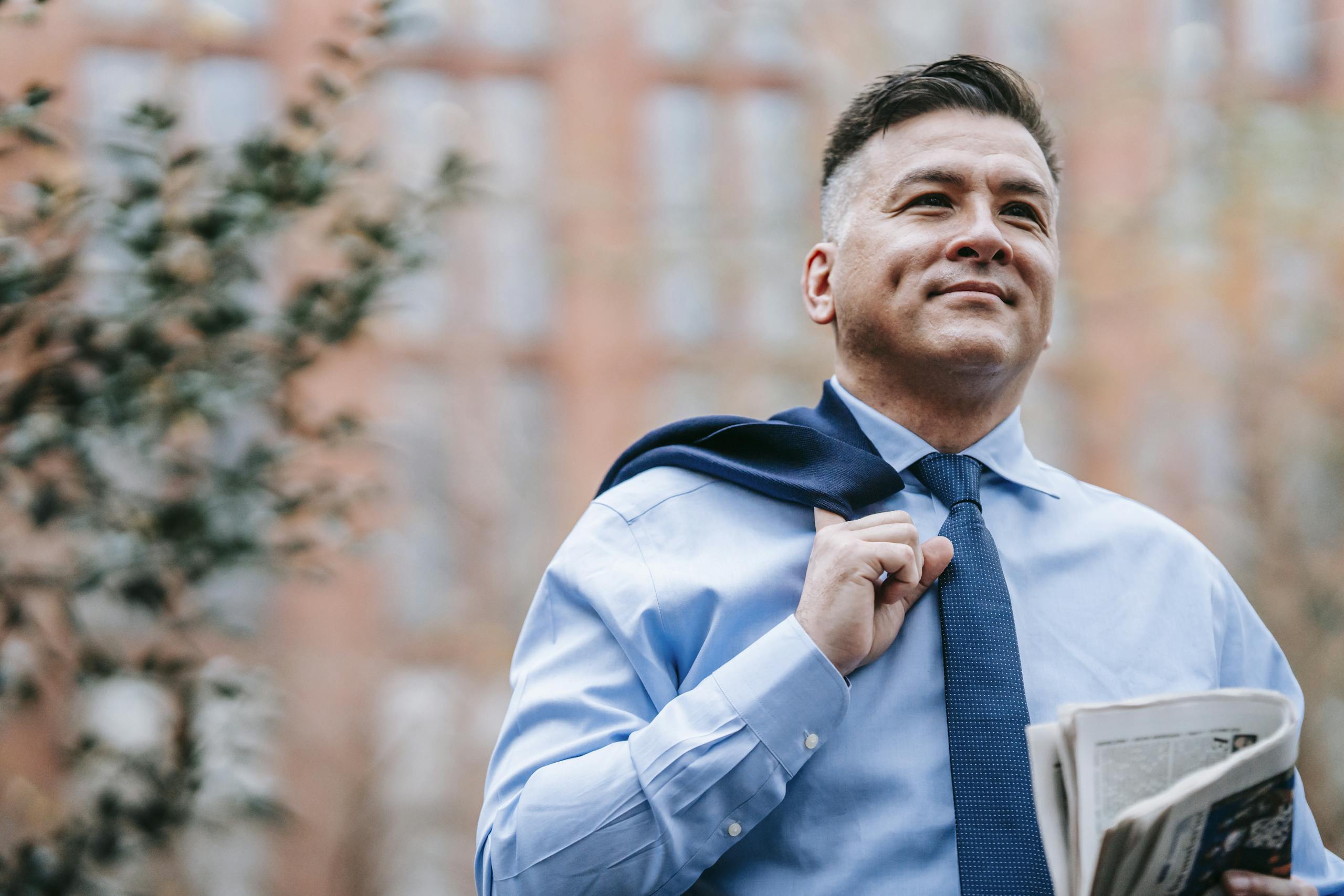 Smiling professional man in formal attire with newspaper, exuding confidence outdoors.