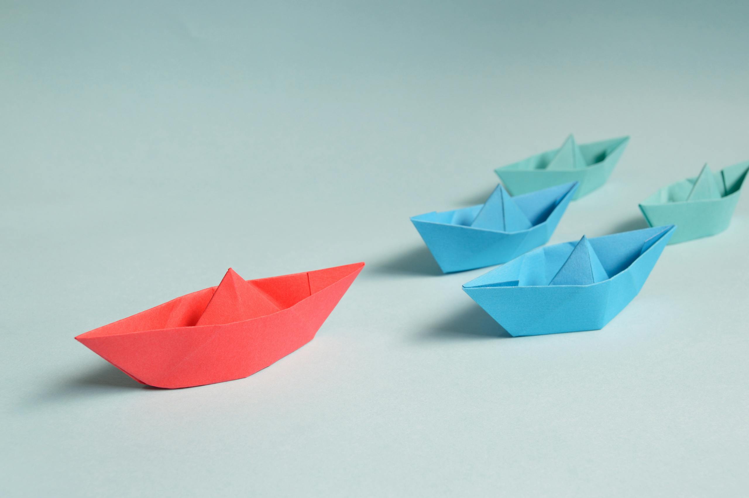 Colorful origami paper boats arranged to depict leadership and teamwork concepts.