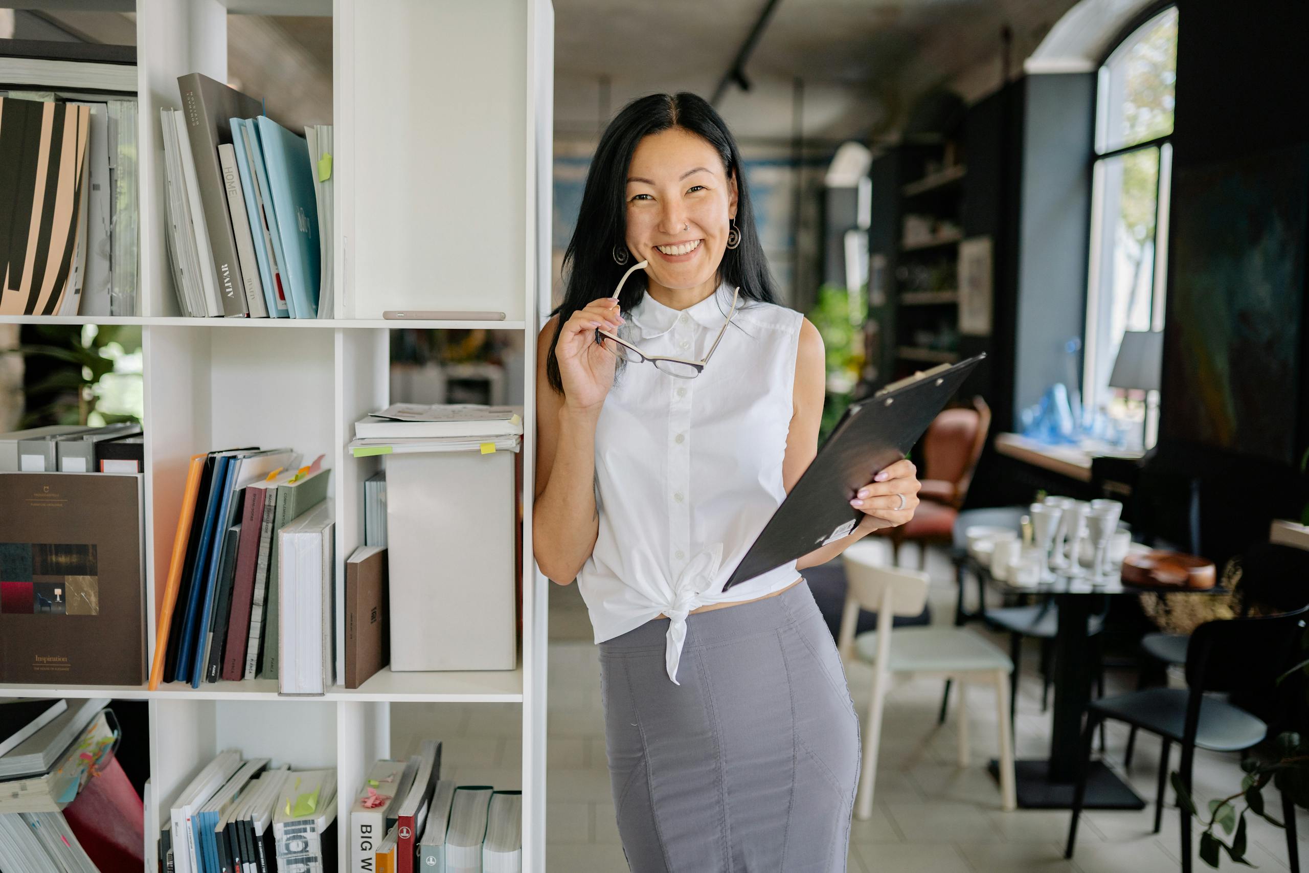 Smiling woman holding eyeglasses and clipboard in a contemporary office.